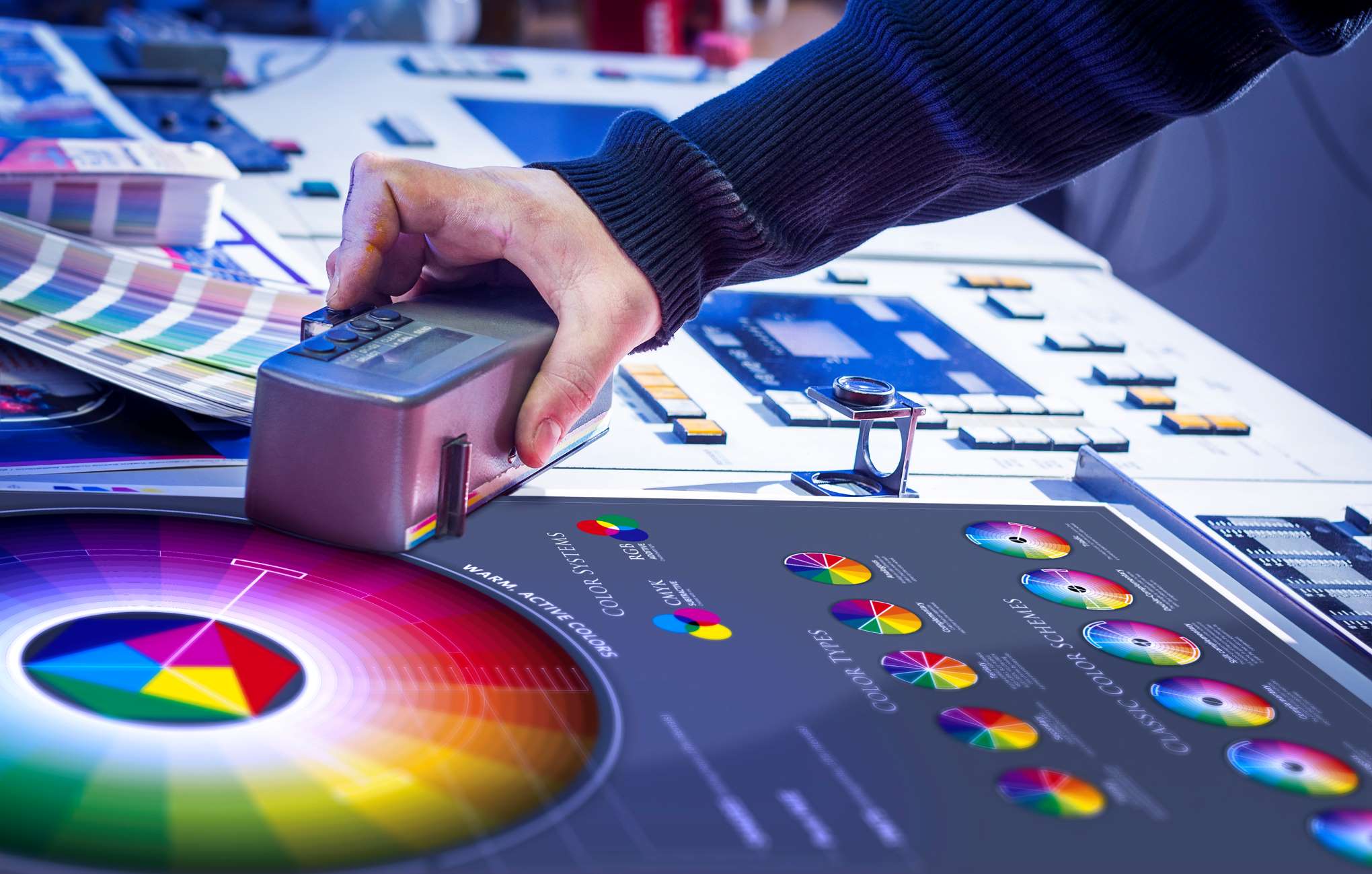 A hand using a spectrophotometer to measure color accuracy on a print sheet, surrounded by color charts and printing equipment.