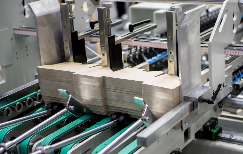 Close-up of an industrial packaging machine processing stacks of folded cardboard boxes in a production line.