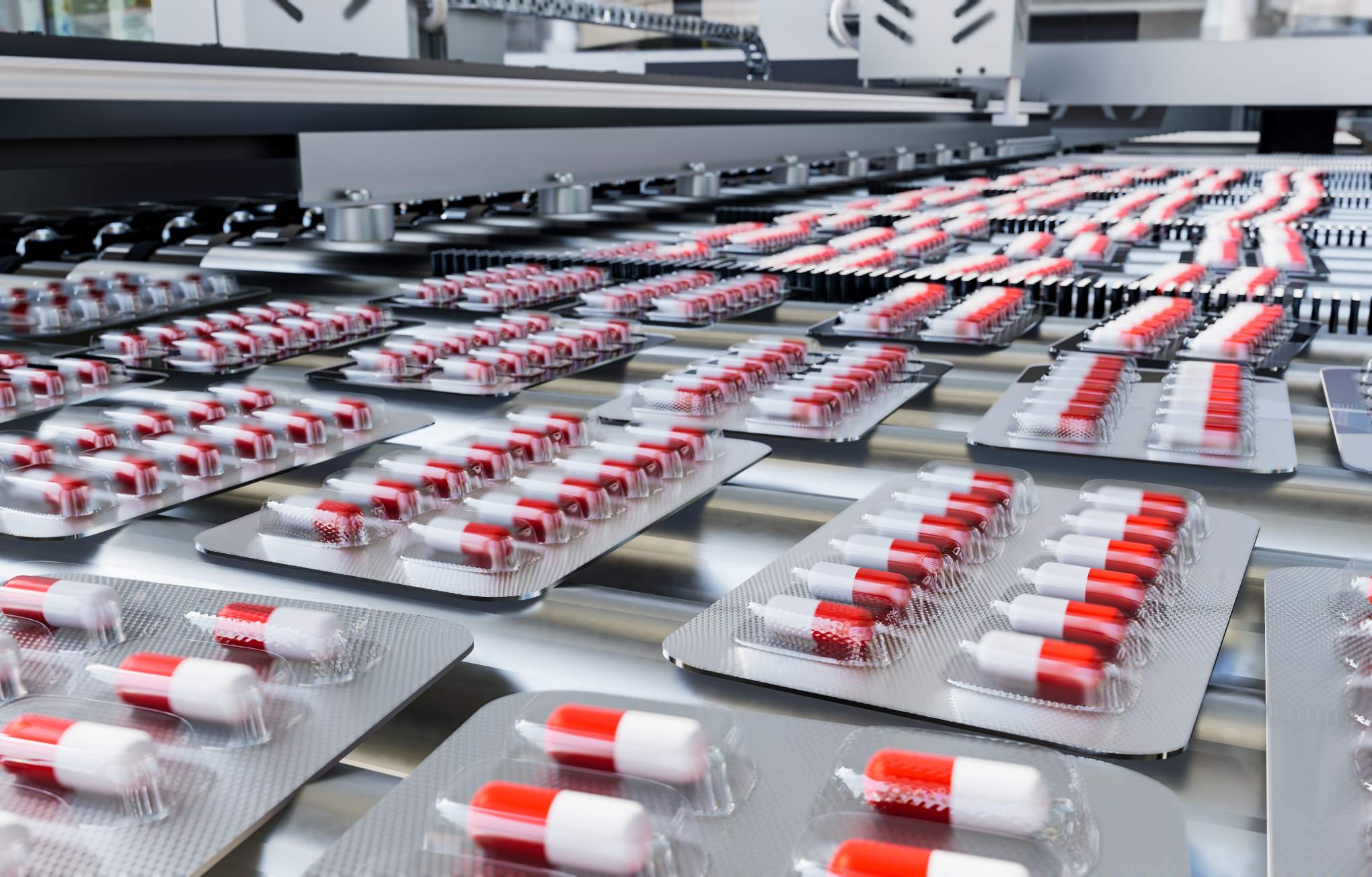 Blister packs of red and white capsules moving along a conveyor belt in a pharmaceutical production line.